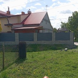 KRIS-STAL - Nowoczesne ogrodzenie z poziomych paneli w kolorze grafitowym, osadzone na betonowych słupkach, na tle domu z czerwoną dachówką i bujnej zieleni.