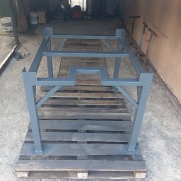 KRIS-STAL - Szara, metalowa konstrukcja spawana na palecie w warsztacie. Element z profili zamkniętych, pomalowany. Widoczne spawy i fragmenty wyposażenia warsztatu w tle.