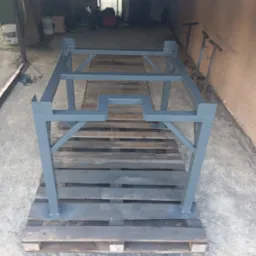 Szara, metalowa konstrukcja spawana na palecie w warsztacie. Element z profili zamkniętych, pomalowany. Widoczne spawy i fragmenty wyposażenia warsztatu w tle.