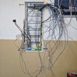 Wattman - Otwarta skrzynka elektryczna w ścianie z wystającymi kablami, widoczne elementy instalacji i narzędzia. Prace w toku, instalacja w trakcie podłączania.