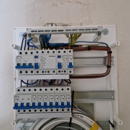 Wattman - Rozdzielnica elektryczna z zamontowanymi bezpiecznikami i przewodami, widok z bliska na ścianie z surowym wykończeniem. Element instalacji elektrycznej w budynku.