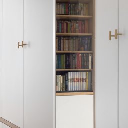 Liczy się wnętrze Justyna Kućmierz - Biała zabudowa meblowa z półkami na książki, otwarte drzwi szafy eksponują regał. Minimalistyczne uchwyty w kształcie litery H. Jasne, stonowane wnętrze.