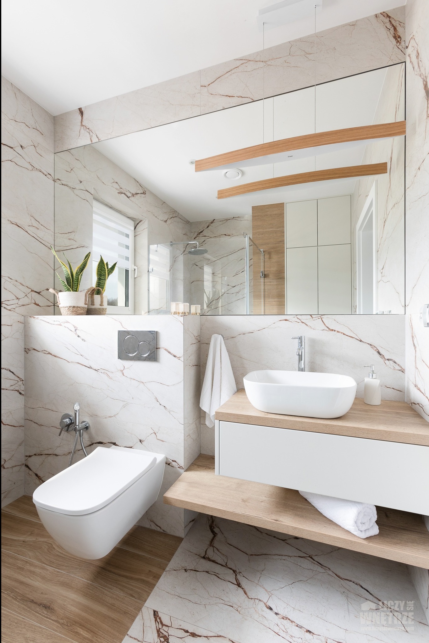 Nowoczesna aranżacja łazienki w Żorach z marmurowymi płytkami, podwieszaną miską WC i umywalką nablatową. W lustrze odbicie kabiny prysznicowej.