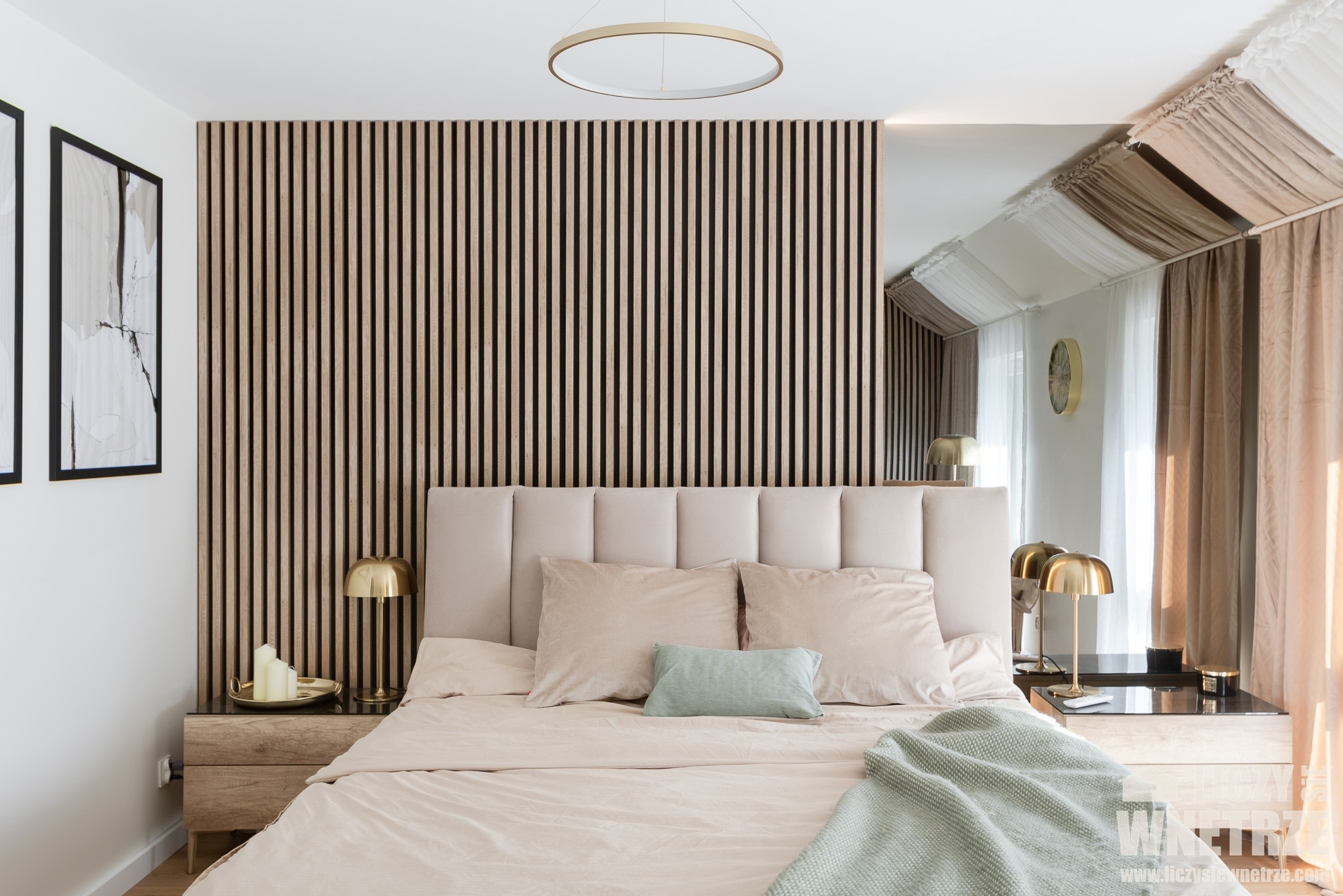 Sypialnia z drewnianą ścianą z lameli, beżowym łóżkiem i złotymi lampkami nocnymi. Lustro odbija okno z zasłonami. Minimalistyczny wystrój.