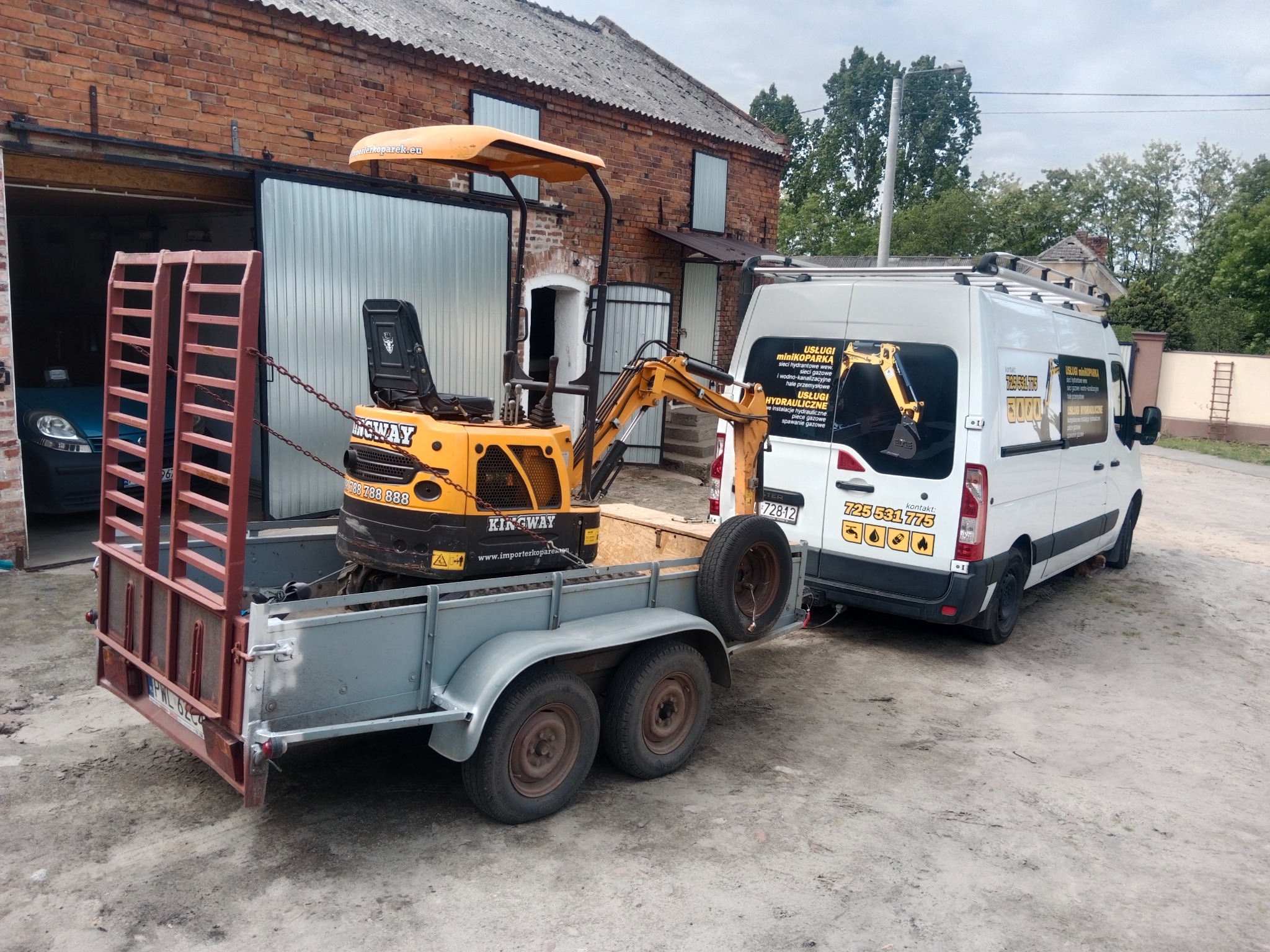 Mini koparka na przyczepie, z naklejką firmy hydraulicznej na białym busie w tle. Widoczne budynki gospodarcze. Sprzęt gotowy do pracy.