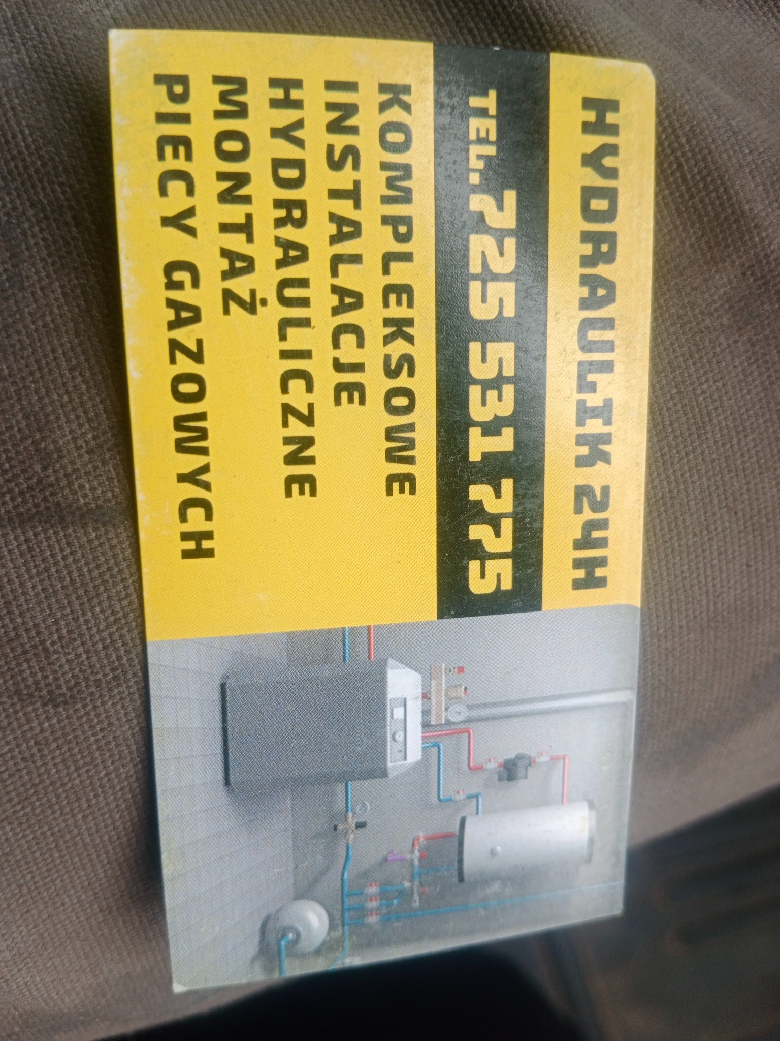 Żółta wizytówka hydraulika z numerem telefonu, oferującego kompleksowe instalacje, montaż pieców gazowych i hydraulikę 24h, z ilustracją instalacji CO.