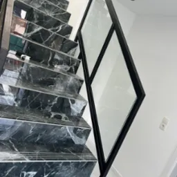 Nowoczesne schody z czarnego marmuru z geometryczną szklaną balustradą z czarną ramą, białe ściany i podłoga, minimalistyczny design.