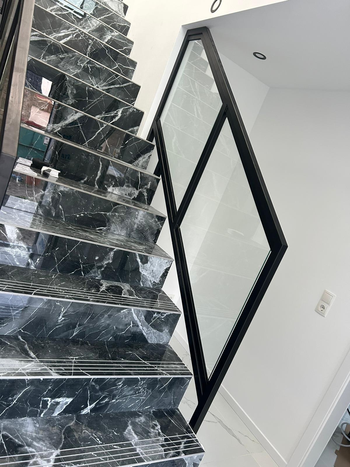 Nowoczesne schody z czarnego marmuru z geometryczną szklaną balustradą z czarną ramą, białe ściany i podłoga, minimalistyczny design.