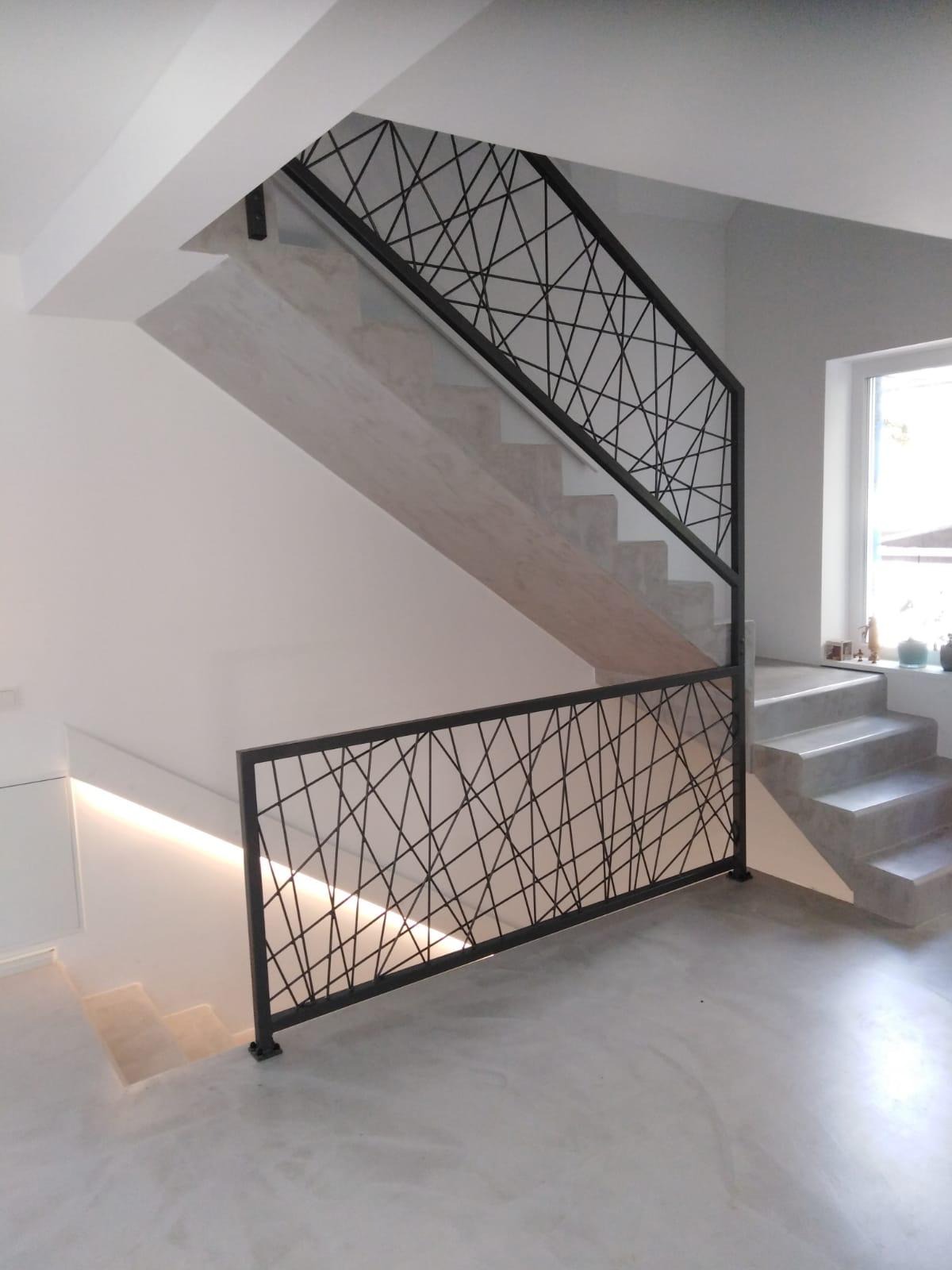 Nowoczesne, geometryczne poręcze schodowe z czarnego metalu, osadzone na betonowych schodach w minimalistycznym wnętrzu z oświetleniem LED. Unikalny wzór.