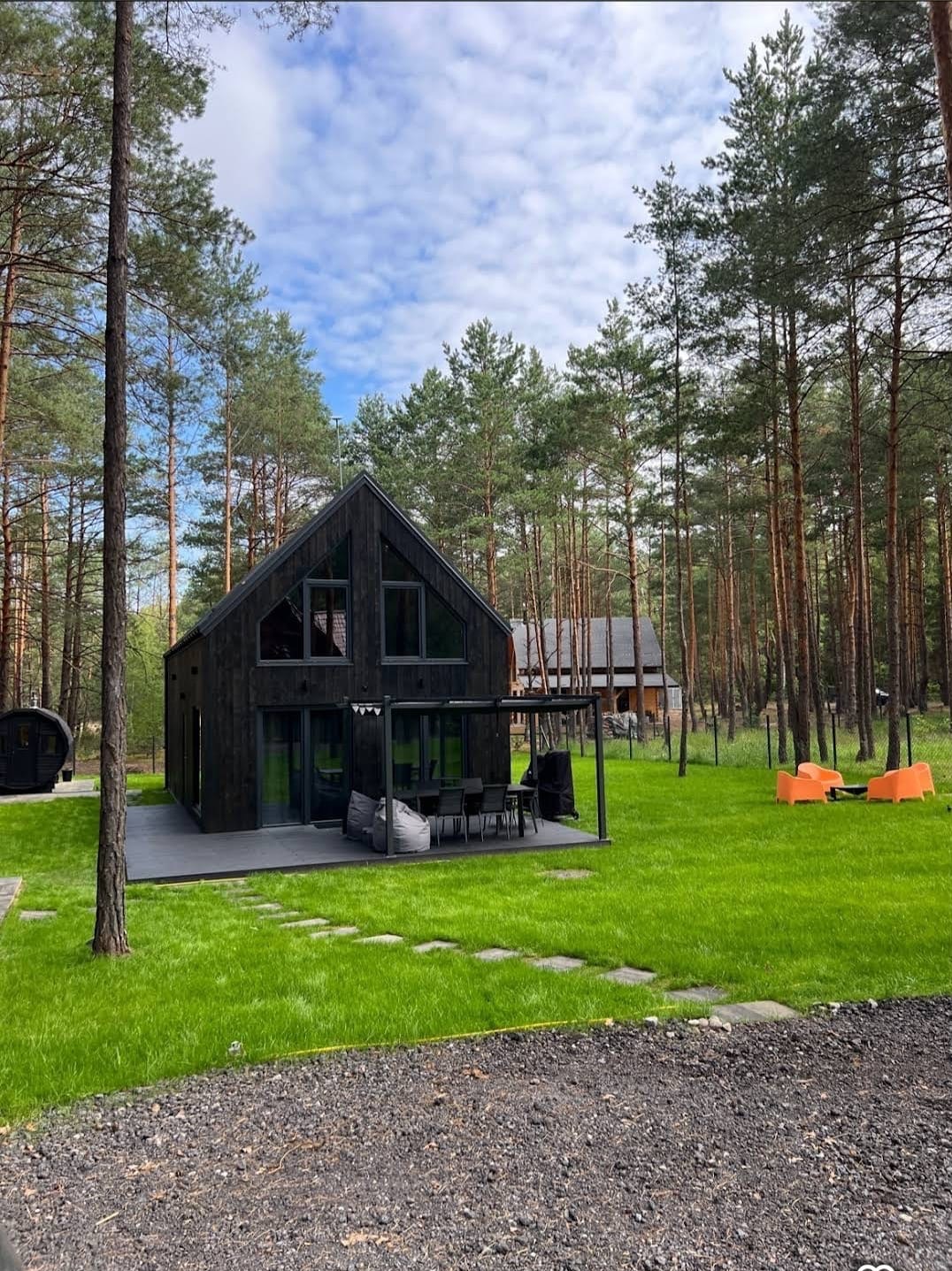 Czarny dom modułowy z dużymi oknami w otoczeniu lasu, z tarasem i meblami ogrodowymi. Realizacja w Pułtusku. Nowoczesna architektura.