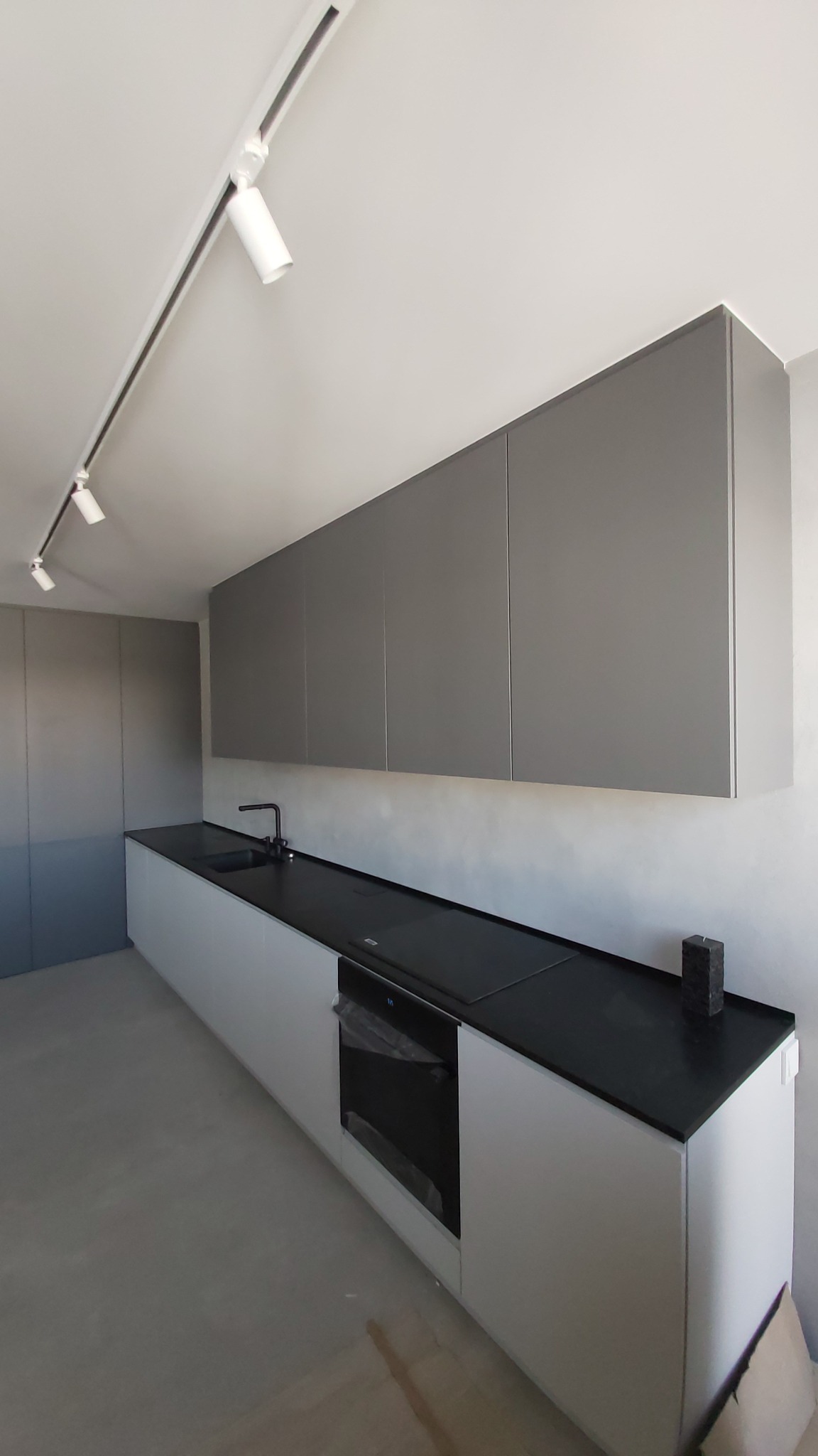 Nowoczesna kuchnia z szarymi szafkami wiszącymi i białymi szafkami dolnymi z czarnym blatem. Minimalistyczny design z oświetleniem punktowym.
