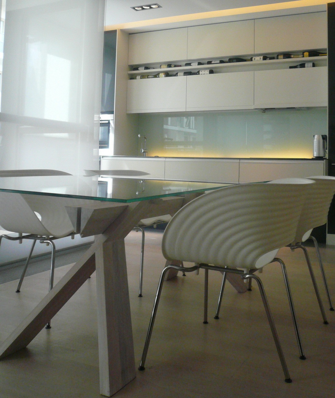 Jasna kuchnia z meblami na wymiar, szklany panel i półka na wino. Szklany stół z drewnianą podstawą i krzesła w stylu skandynawskim. Nowoczesne oświetlenie sufitowe.