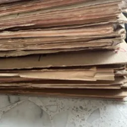 Stos brązowych, postarzanych arkuszy papieru z widocznymi tekstami i grafikami, ułożonych na marmurowym blacie. Detal drukarski.