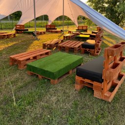 EventHero - Strefa relaksu z palet pod namiotem w Lesznie. Stoliki z zieloną trawą i siedziska z czarnymi poduchami tworzą unikalną przestrzeń eventową.