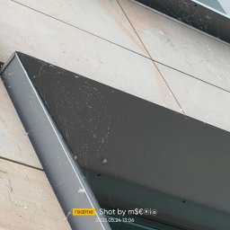 ALPSOLUTIONS SPÓŁKA Z OGRANICZONĄ ODPOWIEDZIALNOŚCIĄ - Z bliska: fragment elewacji z widocznymi pajęczynami i zabrudzeniami na metalowej konstrukcji. Ujęcie z dołu, ukazujące potrzebę czyszczenia.