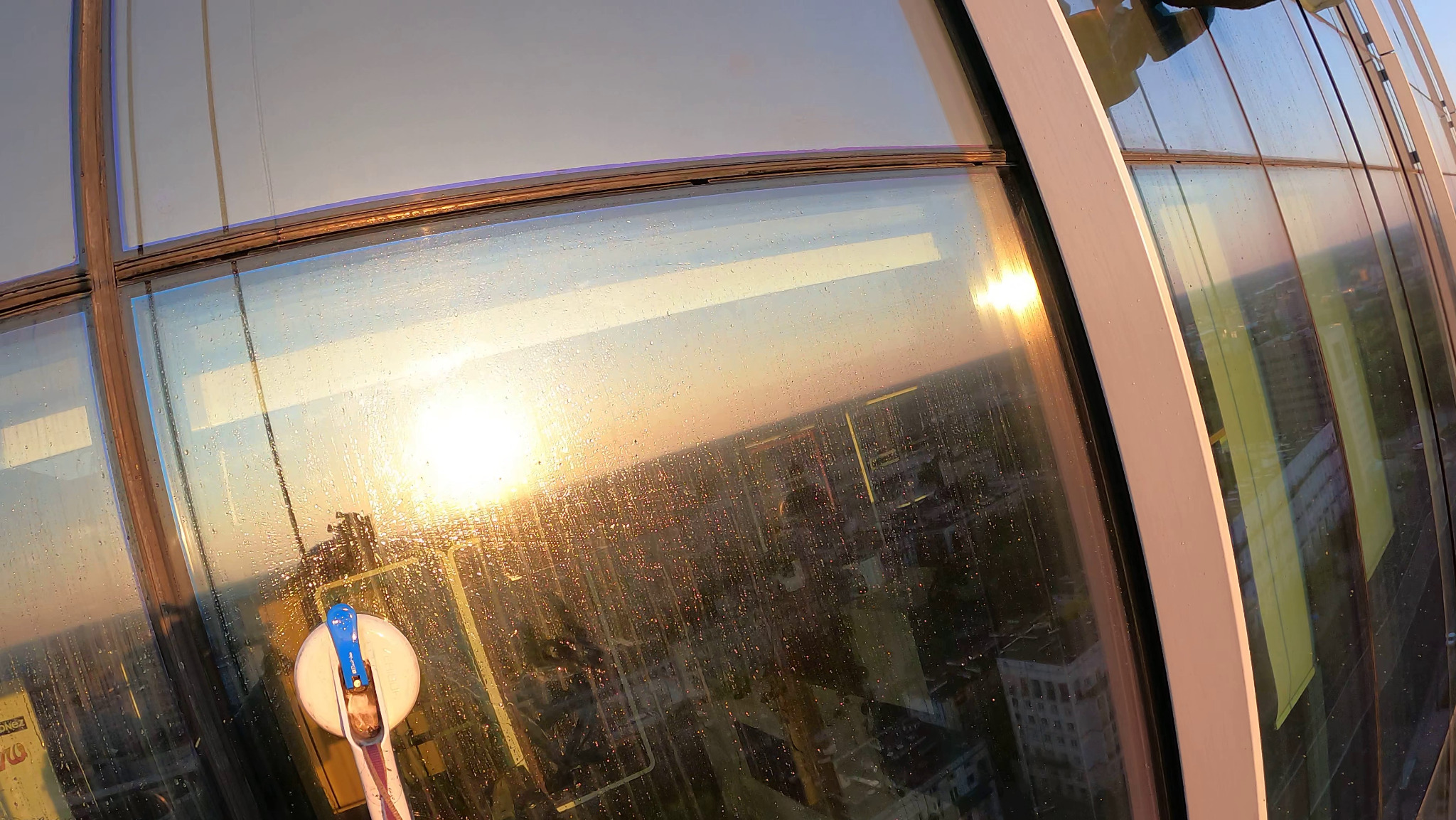 Mycie okien na wysokości w wieżowcu. Widoczna panorama miasta odbijająca się w szybach i narzędzie pracy - myjka do okien z długim uchwytem.