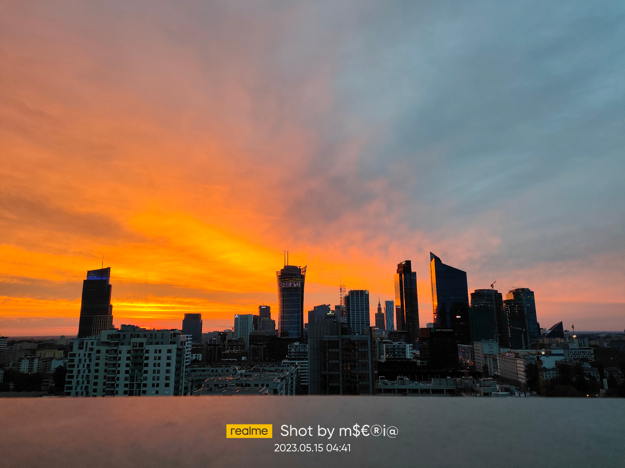 Panorama Warszawy o wschodzie słońca, z widocznymi drapaczami chmur na tle pomarańczowo-szarego nieba. Ujęcie z wysokości, Warszawa.