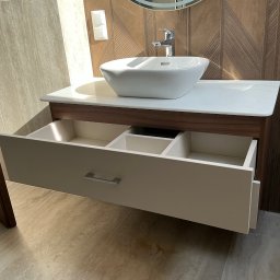 STOLARSTWO - Nowoczesna szafka łazienkowa z otwartą szufladą, białą umywalką nablatową i okrągłym lustrem z podświetleniem na tle ściany z drewnianą okładziną.