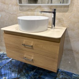 STOLARSTWO - Nowoczesna szafka łazienkowa z umywalką nablatową i chromowaną baterią, na tle marmurowej ściany i podłogi z niebieskiego kamienia.