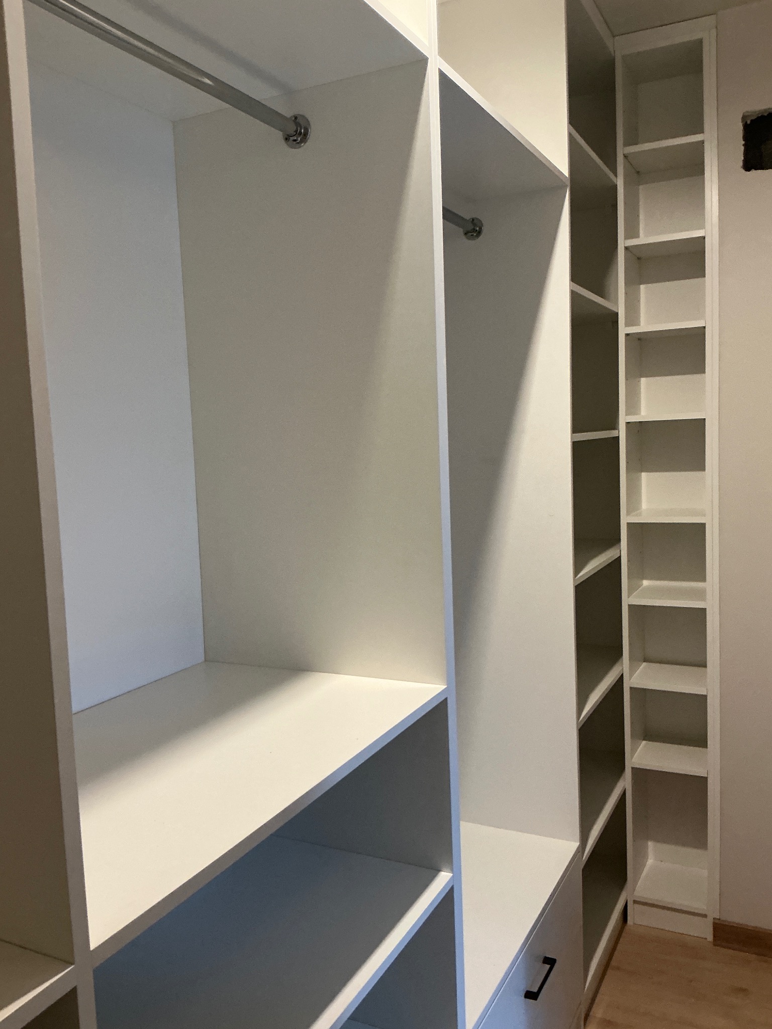 Biała szafa wnękowa z półkami i drążkiem na ubrania, widok z wnętrza. Minimalistyczny design, jasne oświetlenie.