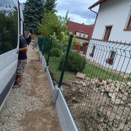 TerraFlo - Montaż ogrodzenia panelowego na betonowej podmurówce, widok z boku na ukończony fragment, obok zaparkowany biały bus. W tle dom z czerwonym dachem.