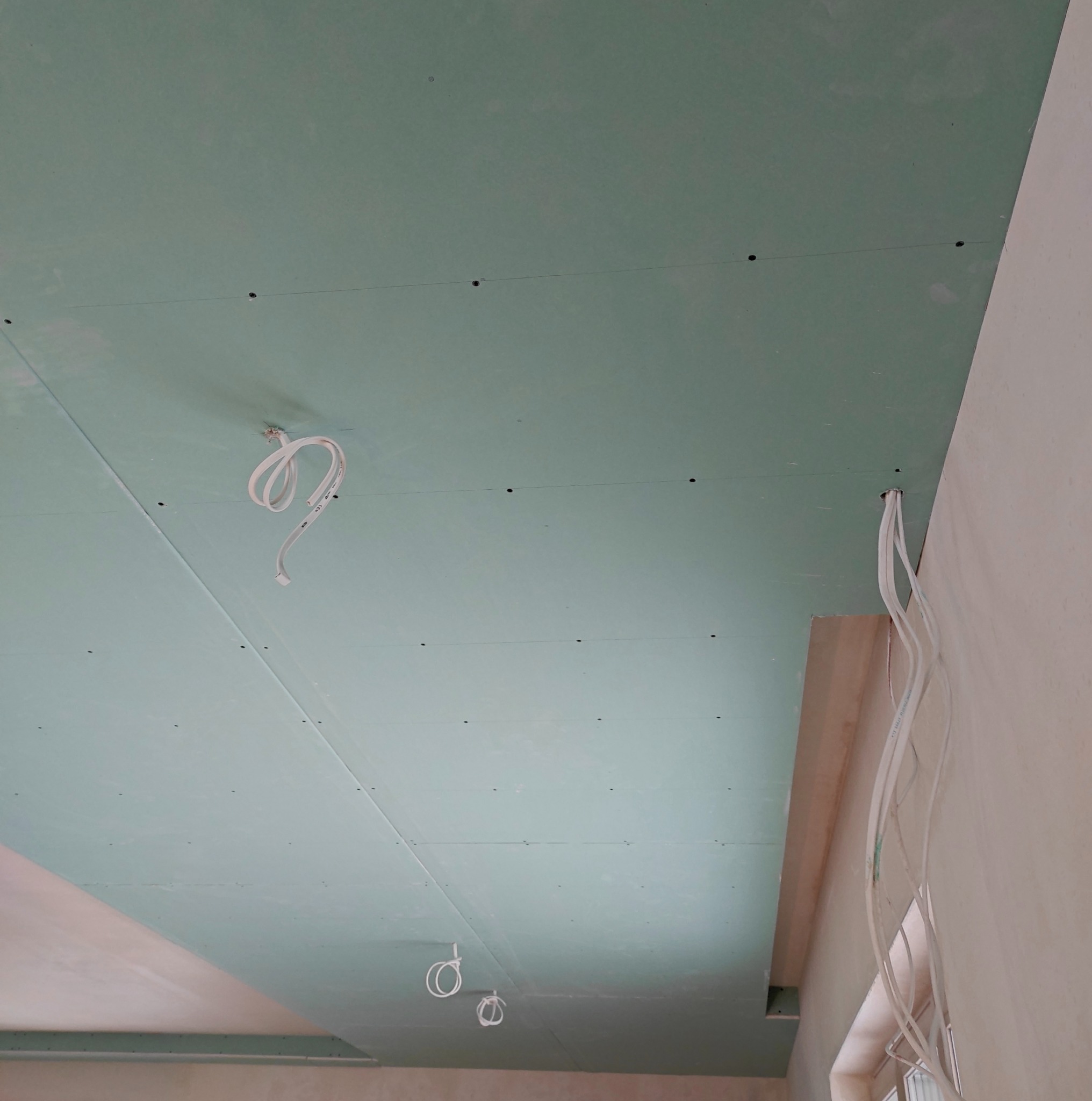 Zielona płyta karton-gips zamontowana na suficie z wystającymi kablami, przygotowana do dalszych prac wykończeniowych. Widoczne łączenia płyt i otwory montażowe.