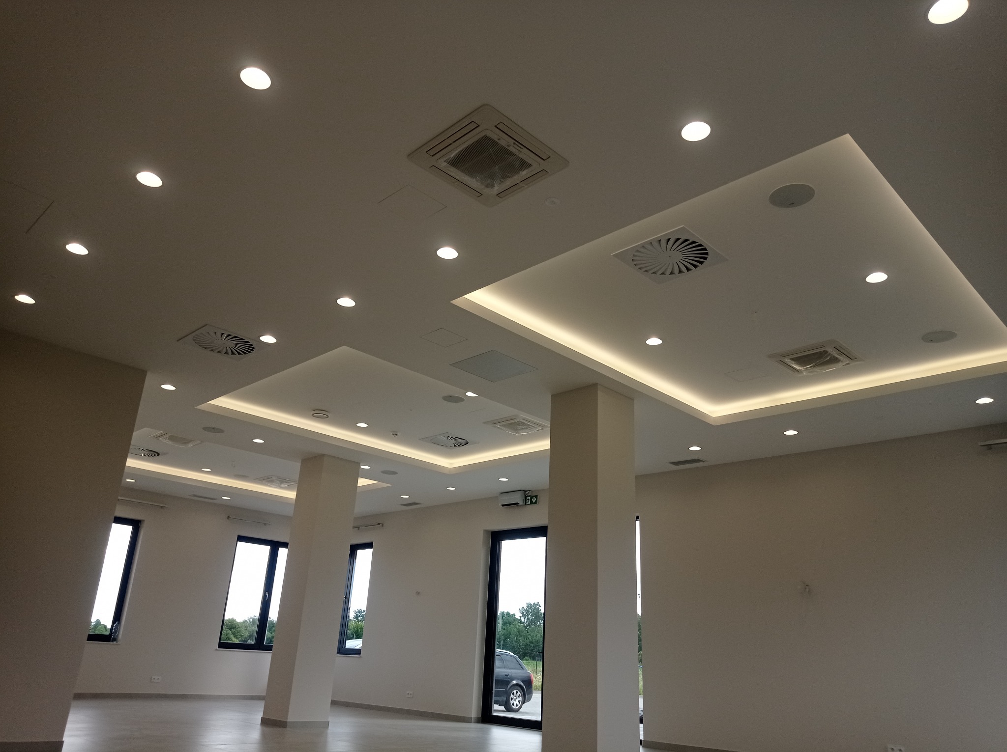 Nowoczesne wykończenie wnętrza biura z podwieszanym sufitem kasetonowym, oświetleniem punktowym i klimatyzacją. Widok na puste pomieszczenie z oknami.