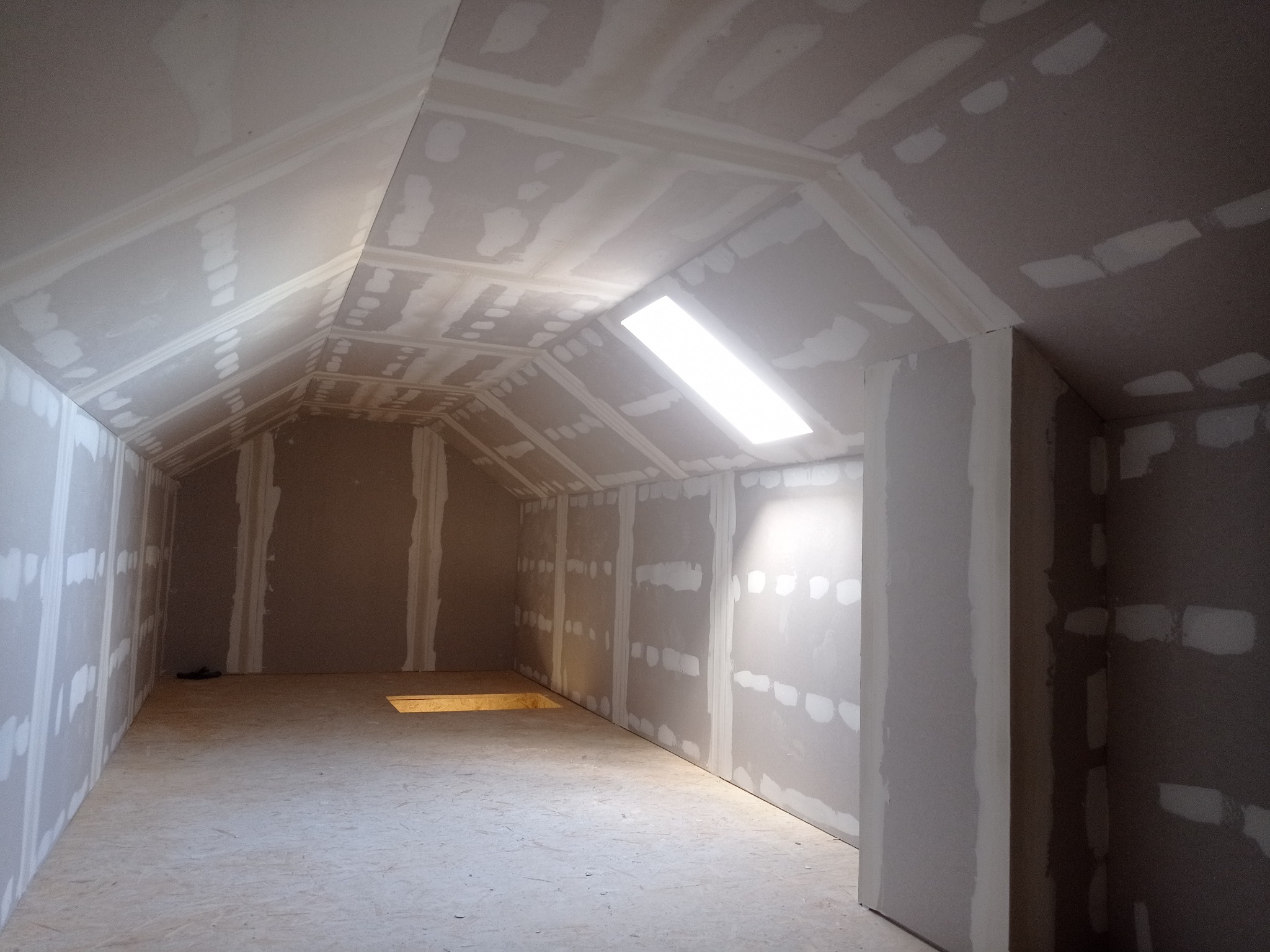 Poddasze w trakcie wykańczania płytami gipsowo-kartonowymi. Widoczne łączenia płyt przygotowane do szpachlowania. Oświetlenie w suficie.