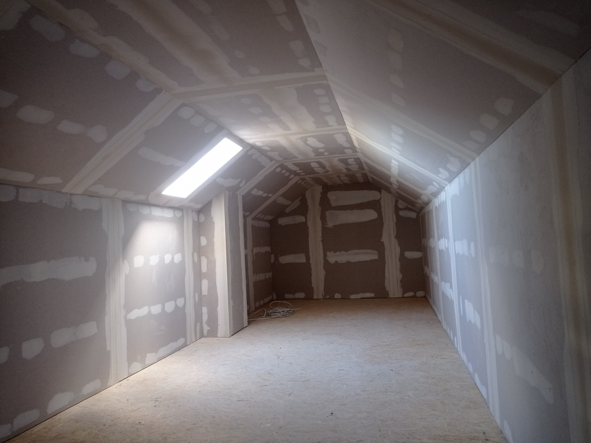 Poddasze z oknem dachowym w trakcie wykańczania płytami gipsowo-kartonowymi. Widoczne łączenia płyt wypełnione masą szpachlową. Surowa podłoga z płyt OSB.