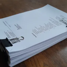 Stos dokumentów prawnych zabezpieczony dwoma klipsami biurowymi na drewnianym stole. Widoczne dane adresowe kancelarii adwokackiej i powodów.