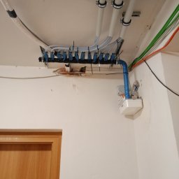 KlimaTech - Rozbudowana instalacja rur i przewodów pod sufitem, z widocznymi elementami mocującymi i różnymi kolorami kabli, sugerująca zaawansowany system instalacyjny w budynku.