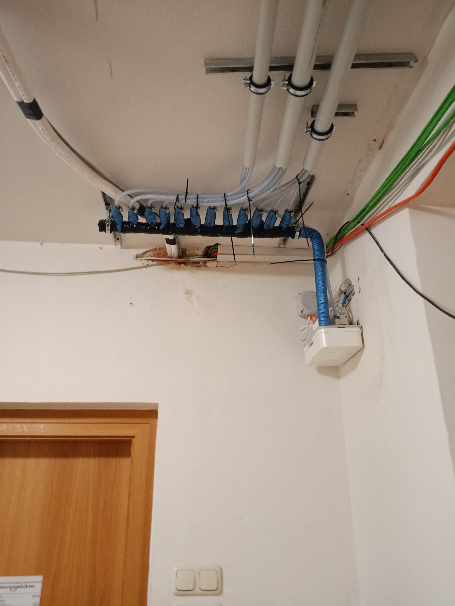 Rozbudowana instalacja rur i przewodów pod sufitem, z widocznymi elementami mocującymi i różnymi kolorami kabli, sugerująca zaawansowany system instalacyjny w budynku.