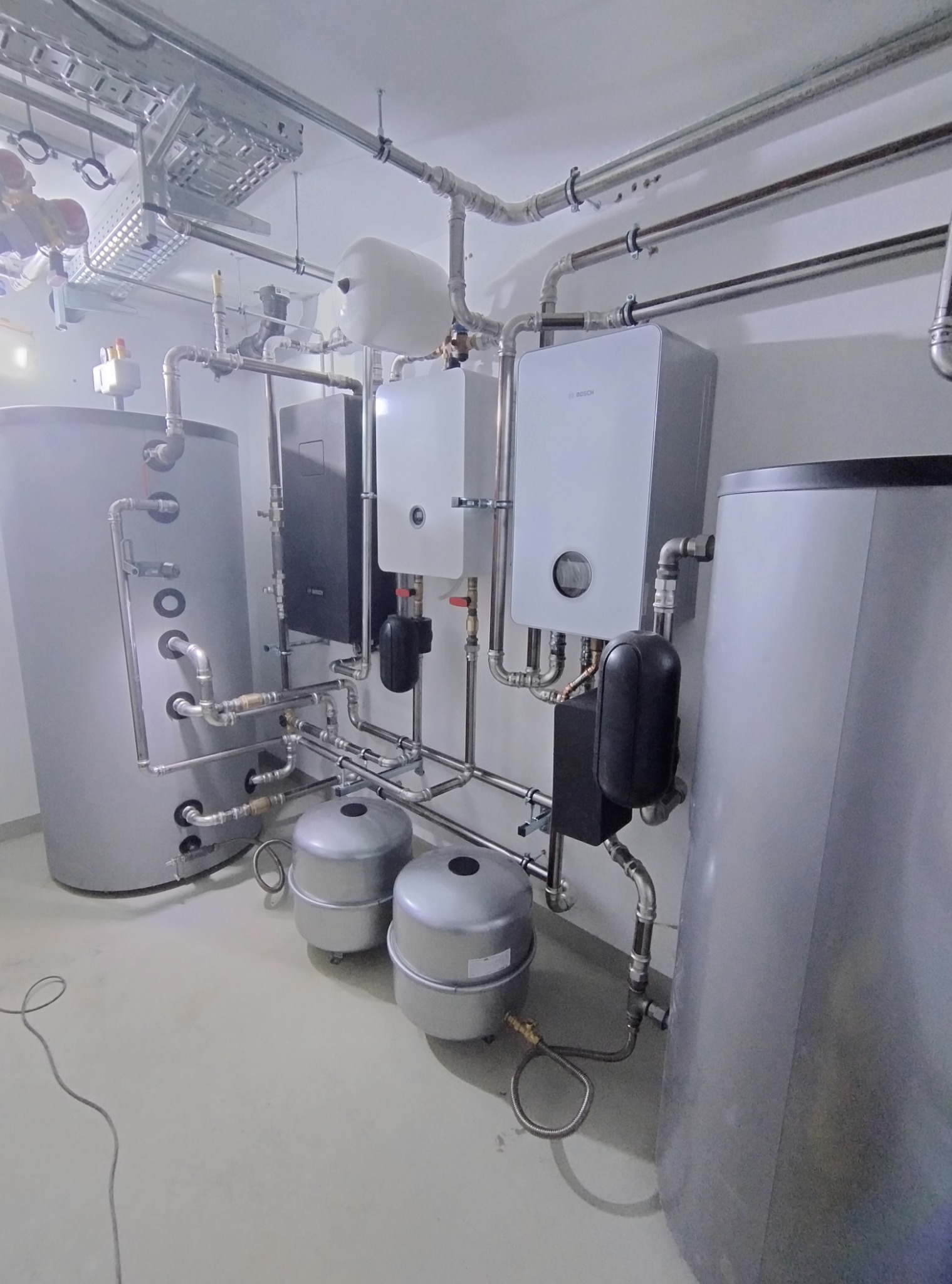 Kompleksowa kotłownia: dwa bojlery, dwa piece gazowe Bosch, zbiorniki wyrównawcze, instalacja hydrauliczna w piwnicy z szynoprzewodami.