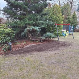 ZK SPÓŁKA Z OGRANICZONĄ ODPOWIEDZIALNOŚCIĄ - Ogród po przekopaniu ziemi pod nasadzenia, z korą wokół drzewa i elementami placu zabaw w tle. Widoczne ślady po pracy glebogryzarki.
