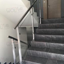 WOLMAR Edyta Wolna - Nowoczesne schody z szarymi, marmurkowymi stopniami i balustradą ze stali nierdzewnej z wypełnieniem szklanym. Widoczne drzwi z numerem 8.