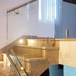 WOLMAR Edyta Wolna - Szklana balustrada z metalowymi poręczami na marmurowych schodach wewnętrznych, oświetlonych punktowo. Widok z dołu, na drugim planie fragment ściany i obraz.