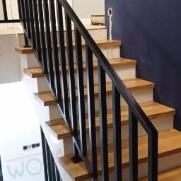 WOLMAR Edyta Wolna - Nowoczesne schody z drewnianymi stopniami i czarną, metalową balustradą o minimalistycznym designie. Widok z dołu, podkreślający geometrię konstrukcji.