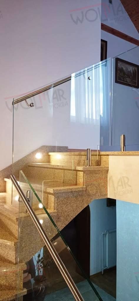 Szklana balustrada z metalowymi poręczami na marmurowych schodach wewnętrznych, oświetlonych punktowo. Widok z dołu, na drugim planie fragment ściany i obraz.