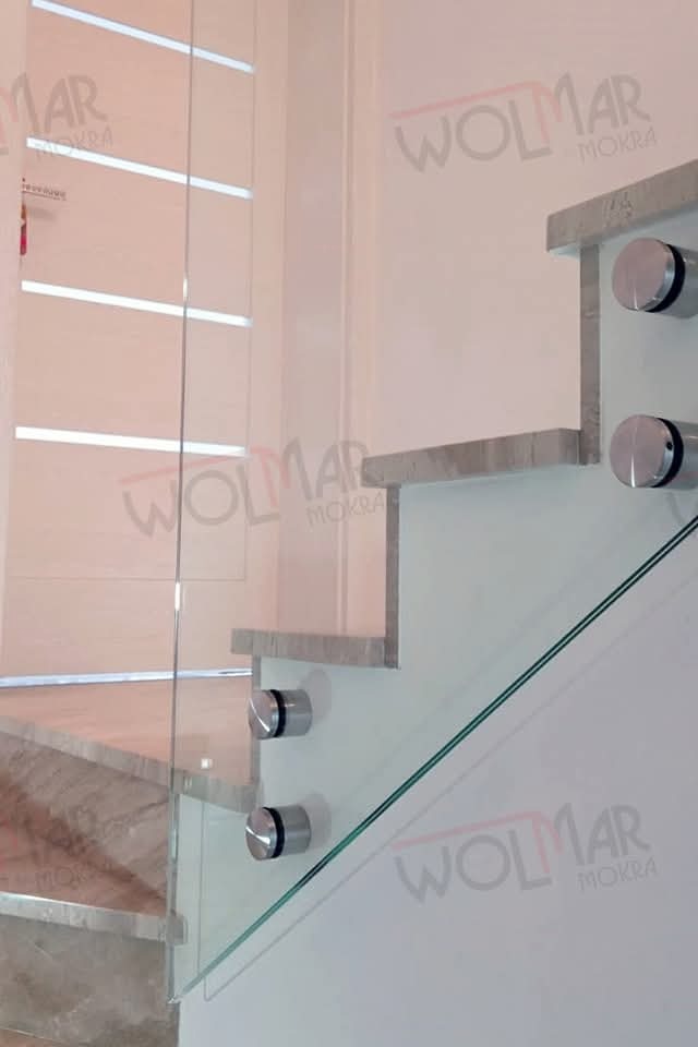 Szklana balustrada schodowa z marmurowymi stopniami i srebrnymi mocowaniami. Widoczne logo firmy na ścianie. Detal nowoczesnego wykończenia wnętrza.