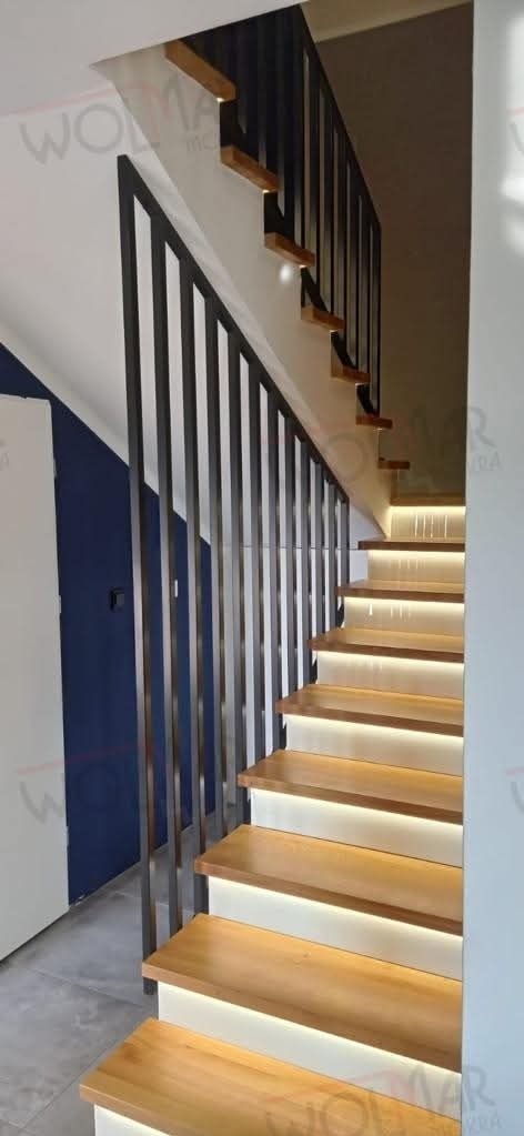 Nowoczesne schody drewniane z metalową balustradą o pionowych szczeblach, podświetlane od spodu. Widok z dołu, z boku. Minimalistyczny design.
