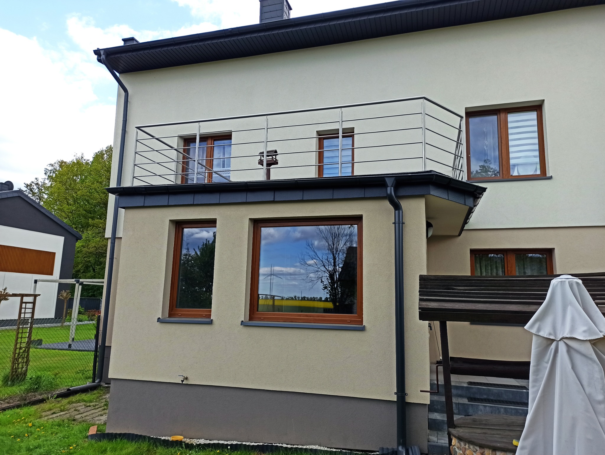 Nowoczesna balustrada balkonowa ze stali nierdzewnej w Mokrej, z widoczną karmnikiem dla ptaków, zamontowana na budynku z oknami z brązowymi ramami.