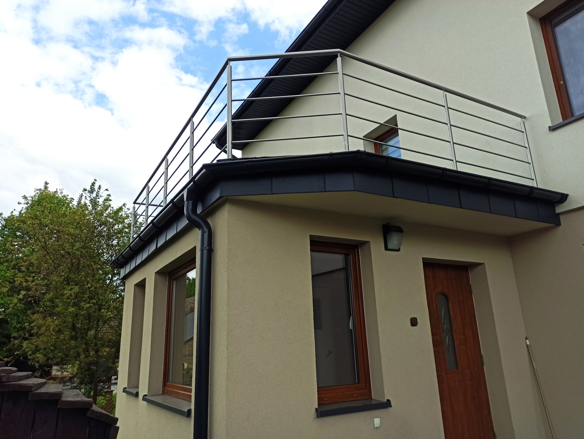 Nowoczesna, pozioma balustrada ze stali nierdzewnej na balkonie domu jednorodzinnego, widok z dołu, błękitne niebo w tle. Minimalistyczny design.