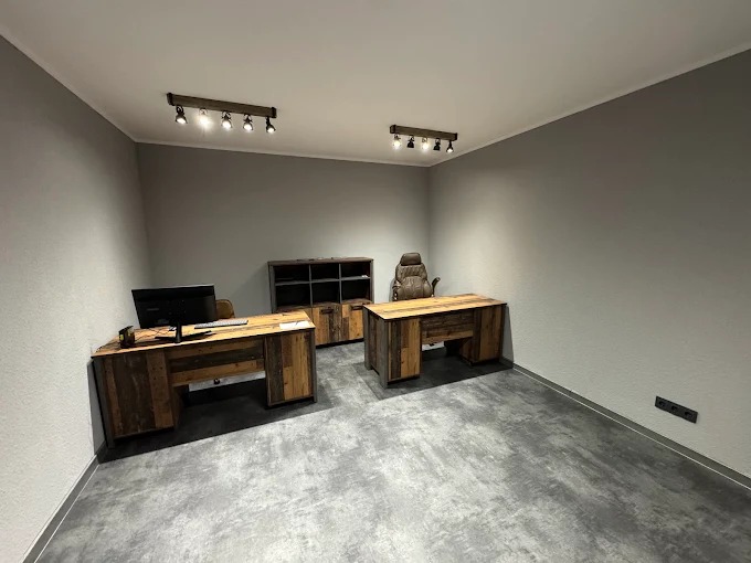 Nowoczesne biuro z dwoma biurkami z drewna odzyskanego, regałem i skórzanym fotelem. Oświetlenie punktowe na suficie. Szare ściany i podłoga z betonu architektonicznego.