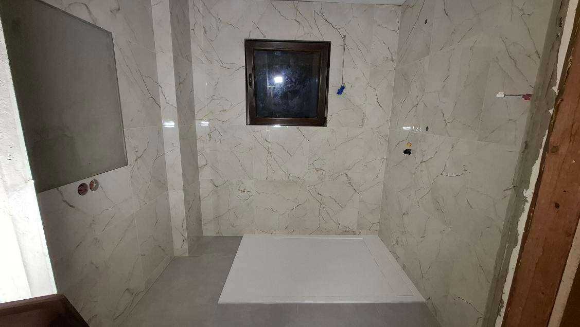 Wykończona łazienka w Kosarzewie Dolnym z marmurowymi płytkami, brązowym oknem i białym brodzikiem. Widoczne przygotowane punkty instalacji.