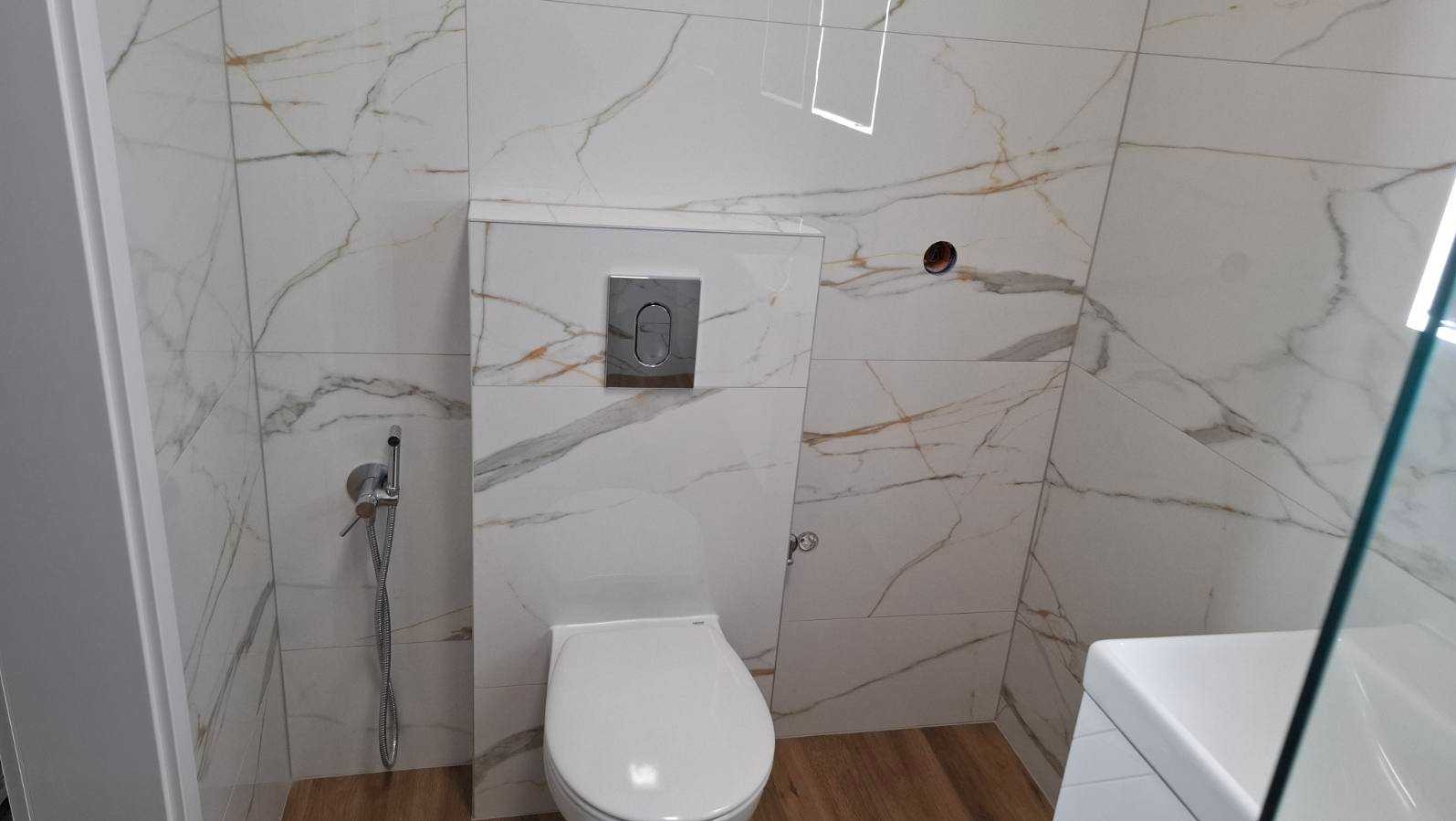 Wykończona łazienka z toaletą podwieszaną i bidetką. Płytki imitujące marmur z złotymi żyłami na ścianach i drewnopodobna podłoga. Nowoczesny design.