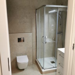 Zakład Remontowo Budowlany ART-DOM Dariusz Sajnóg - Nowoczesna łazienka z beżowymi płytkami, kabiną prysznicową i podwieszaną toaletą. Minimalistyczny design z akcentami chromu i białymi meblami.