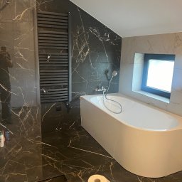 Zakład Remontowo Budowlany ART-DOM Dariusz Sajnóg - Nowoczesna łazienka z czarnymi płytkami imitującymi marmur, białą wanną i grzejnikiem drabinkowym. Okno z czarną ramą doświetla wnętrze.