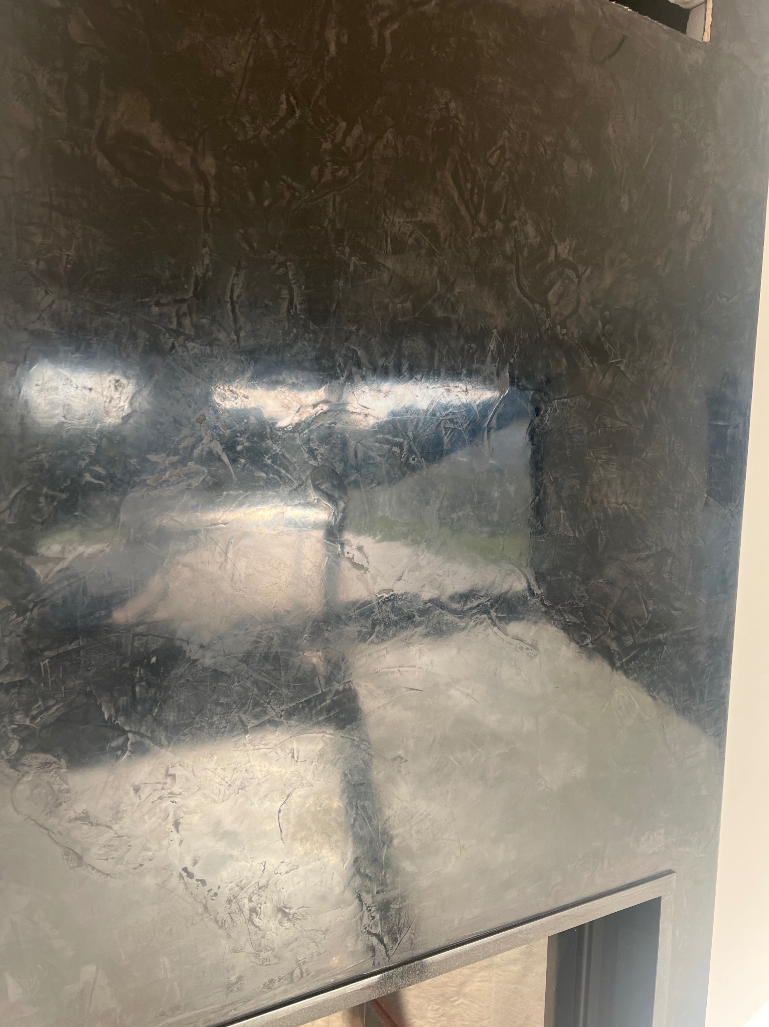 Ściana z efektem dekoracyjnym w odcieniach szarości i srebra, imitująca metaliczne wykończenie. Widoczna faktura i refleksy świetlne. Fragment obudowy kominka.