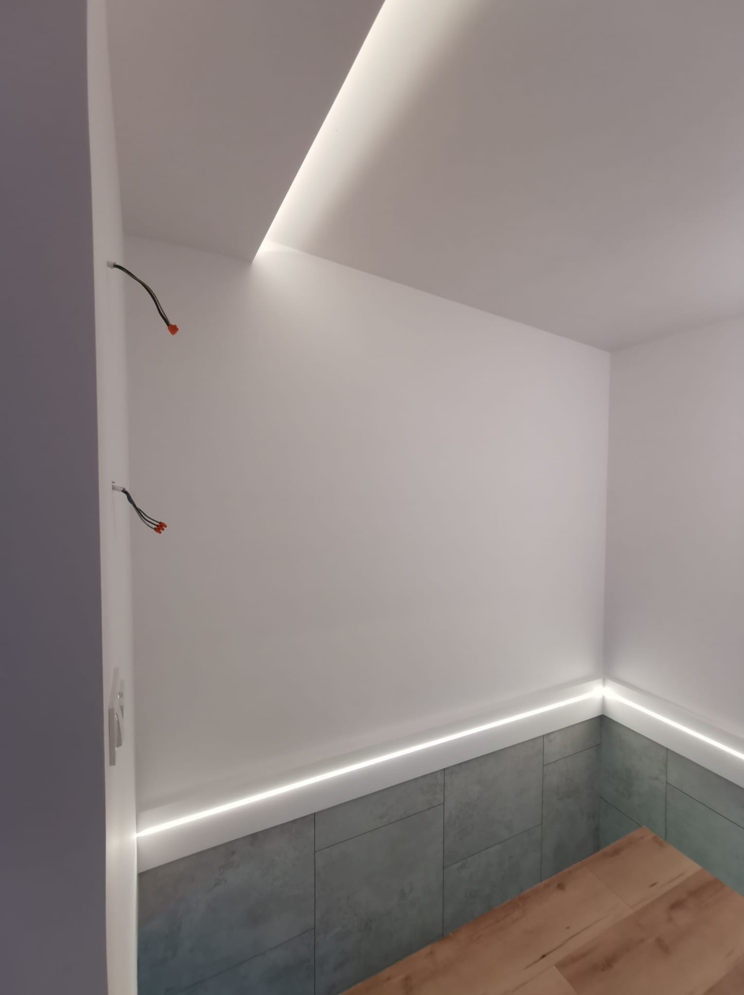 Nowoczesne oświetlenie LED w łazience: listwa sufitowa i przypodłogowa. Widoczne kable elektryczne. Płytki imitujące beton i drewnopodobna podłoga.