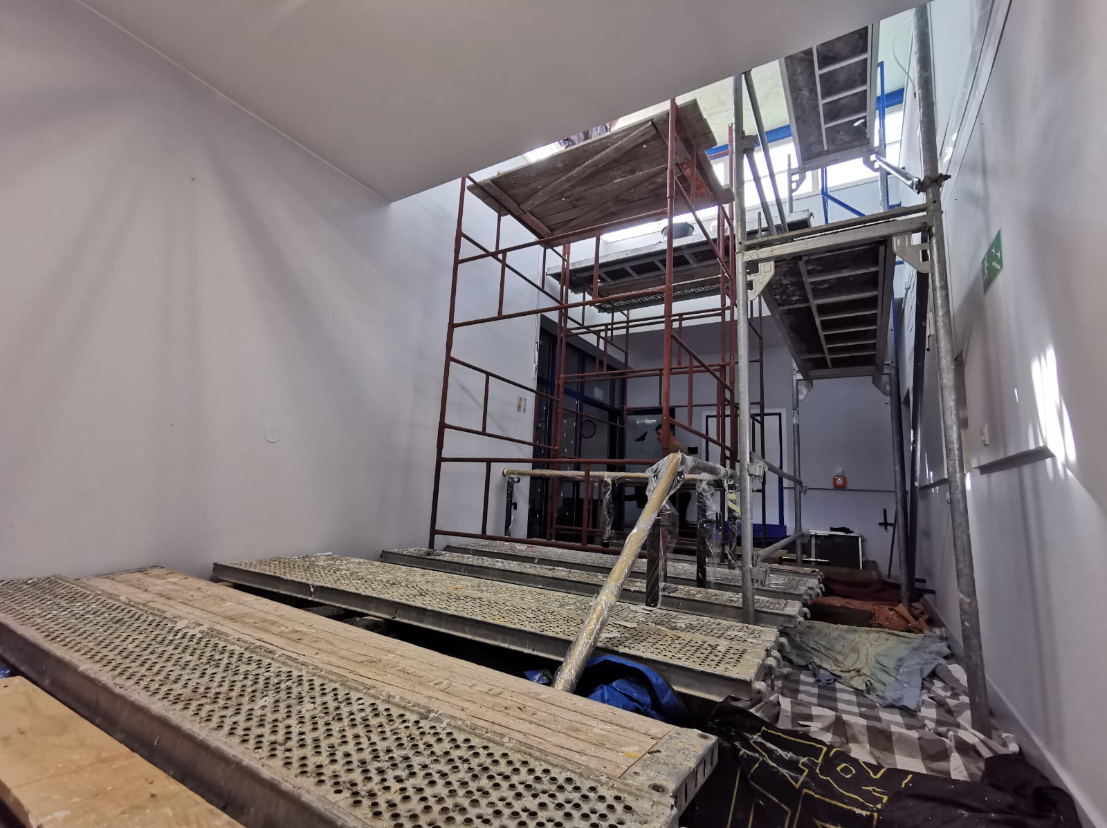 Wnętrze w trakcie malowania: białe ściany, rusztowania metalowe, widoczny pracownik. Przygotowanie do malowania w wysokim pomieszczeniu z oknem dachowym.